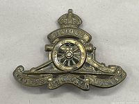 Close-up front view of one vintage King's Crown Royal Artillery cap badge. Shows detailed cannon wheel, crown, and inscriptions on banners.