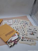 Large assortment of stamps including loose stamps in envelopes and several collection album pages with mounted stamps.