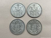 Top-down view of all four 50 cent coins showing the reverse side with the Canadian coat of arms and dates 1939, 1952, 1955 (two coins).