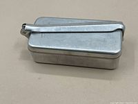 Closed rectangular metal sterilizing box with hinged locking arm on the top.