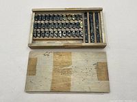 Top view of the wooden box open showing arranged metal semi-circular inserts and rectangular text inserts.