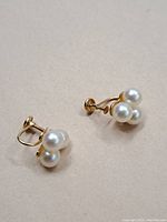 Pair of vintage 14k gold earrings with three white pearls each, showing screw-back mechanism and cluster design.