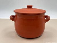 Full front view of a terracotta bean soup pot with handles and lid on top, showing orange-red glazed surface.