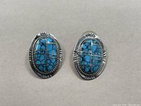 Front-facing view of the pair of oval sterling silver earrings with turquoise inlay showing engraved silver border and segmented turquoise stones.
