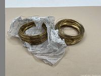 Two coils of thin gauge brass wire laid flat on plain background, one partially wrapped in paper, showing overall condition and color.