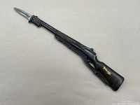 Full view of a rifle-shaped cast metal letter opener with a silver blade and dark body.