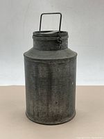 Front view of the full milk can showing cylindrical body, bail handle, and lid with latch.
