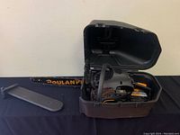 Photo of Poulan Pro PR4218 gas chainsaw inside open black and brown hard plastic case with bar cover placed beside it on table.