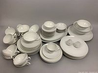 Overview of entire grouping showing cups, saucers, plates, bowls and platters arranged on gray surface