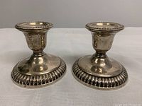 Front view of the two sterling silver weighted candleholders placed side by side on a white textured surface.