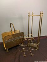 Three brass home accessories together: umbrella stand, magazine rack, and wine rack