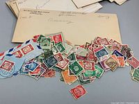 Photo of loose vintage postage stamps spread on table with manila envelope labeled 'Cayman' visible