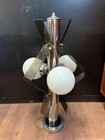 Front view of atomic style lamp with chrome cylindrical base, three white glass globe bulbs and smoked lucite angular panels.