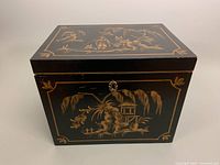 Front angle showing gold hand-painted Chinese landscape scene on black box with hinged lid.