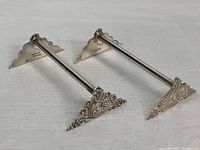 Side view of two sterling silver knife rests showing the engraved sterling mark and intricate design on the triangular supports.