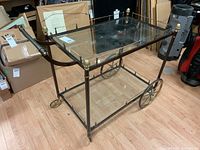 Front view of entire metal and glass bar cart showing frame, trays and wheels