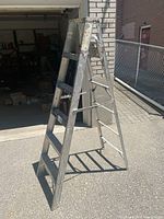 Aluminum step ladder standing unfolded, showing side steps and fold-out leg for support.