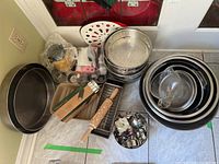 Overview of all items including stainless steel bowls stacked nested, bakeware pans, rolling pin, metal utensils, and Pampered Chef bread tube box.