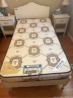 Top-down view of twin mattress on white wood veneer bed frame showing surface pattern and mattress labels