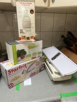 Three boxed and unboxed food slicing and chopping tools including Starfrit fry cutter and cuber, Euro Chopper vertical chopper, and a white mandolin slicer.