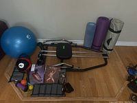Photo showing entire lot including rowing machine, stability ball, kettlebell, ankle weights, massage ball, yoga mats, books and VHS tape.