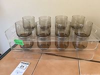 Twelve smoked glass cups arranged on two clear acrylic trays, six glasses per tray.