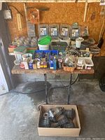Wide table view showing multiple small hardware items including screws, fasteners, hooks, plastic bags with fittings, and a box containing solar patio lanterns in bottom foreground.