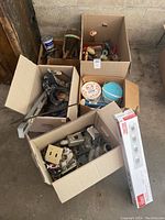 Boxes filled with various painting and DIY supplies including brushes, rollers, paint cans, clamps, and putty tools.
