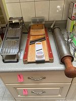 Overview photo of mandolin slicer, cabbage shredder, plastic peeler and sausage stuffer with wooden handle on kitchen countertop.
