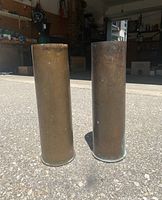 Two large empty metal shell casings standing vertically on concrete floor in front of an open garage, showing aged surfaces and patina.