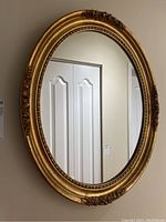 Full view of the oval wall mirror showing the gold gilt frame and clear reflective glass.