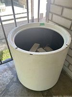 Close-up front view of round white plastic planter pot filled with several light gray rectangular bricks and potting soil inside, some wear visible.