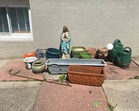 Full lot display outdoors showing all items including Madonna statue, various planters, and watering cans