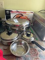 Front angled view of entire set showing roaster, two pots with lids, small bowl, and original box.
