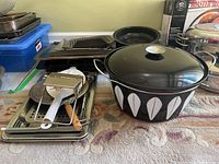 View of the full lot showing the enamel roaster and various trays stacked behind with kitchen utensils visible on trays.