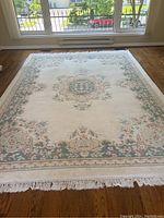 Full view of the rectangular wool rug laid flat on hardwood floor, showing central medallion and border with floral designs and fringe.