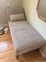 Chaise lounge from top view showing textured beige upholstery and wooden legs, with a rectangular pillow on it.