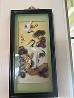 Full view of Asian shadow box with cranes, pine trees, and Asian characters under glass in black frame