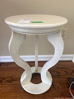Front view of the white wood side table showing round top and sculptural curved pedestal base.