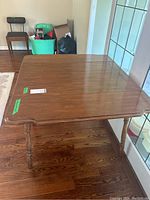 Photo showing wooden table top with two drop leaves, medium brown finish, placed on wooden floor.