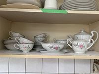Shelf view showing cups, saucers, soup bowls, sugar bowls, and plates with floral pink rose design