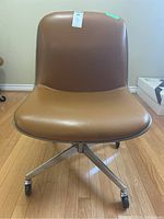 Front view of vintage Steelcase slipper chair showing brown faux leather seat and backrest on chrome base with wheels.