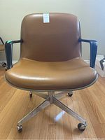 Front view of vintage Steelcase rolling desk chair with brown faux leather seat, black plastic arms, and chrome base with wheels