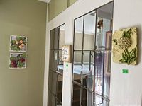 Photo showing three ceramic wall plaques mounted on a wall next to a mirrored closet door, displaying different fruit and floral designs.