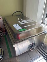 Photo of large stainless steel electric warming tray with lid showing control dial at front and electrical cord at back.