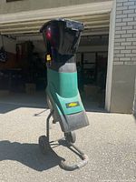 Front-side view of green and black Yardworks electric mulcher on wheels with yellow latch, outdoors by garage.