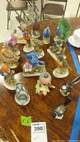 Overview showing 16 porcelain bird figurines on wood table, various sizes and brands, bases with floral or leaf designs.