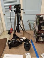 Full kit including Nikon D70 camera body, Nikon lens, tripod, battery, and charger on table.