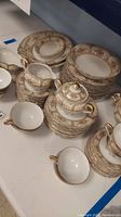 Full set arranged showing plates stacked, cups, teapot and creamer, illustrating the full china set with floral pattern and gold trim.