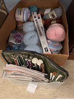 Top view of box showing multiple skeins of colorful yarn, knitting needles in roll, and pattern booklets.
